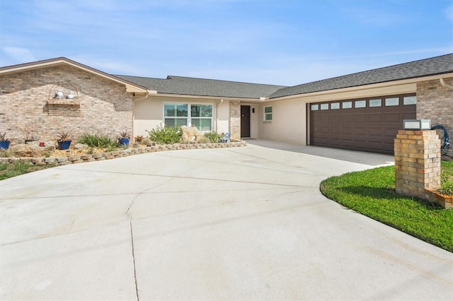 ranch-style house featuring an attached garage, concrete driveway, brick siding, roof with shingles, and stucco siding