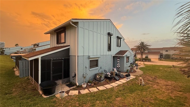 1766 Windsong Cir, Flagler Beach, FL 32136 - back of house at dusk with a sunroom, a lawn, and board and batten siding