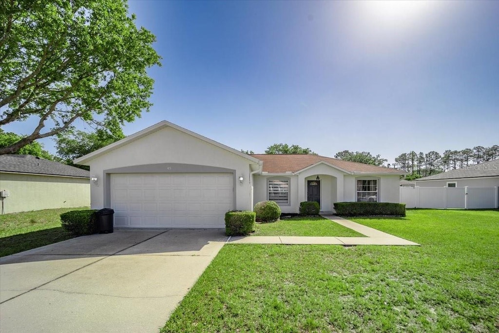 view of front facade featuring a garage, fence, stucco siding, a front lawn, and driveway