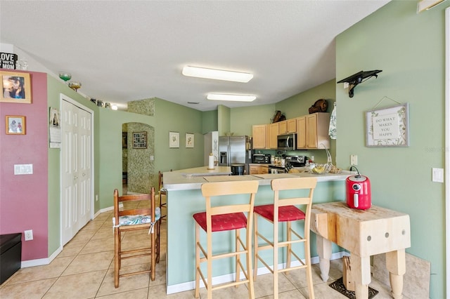 42 Buffalo Bill Dr, Palm Coast, FL 32137 - kitchen with light tile patterned floors, a kitchen breakfast bar, a peninsula, light brown cabinetry, and stainless steel appliances