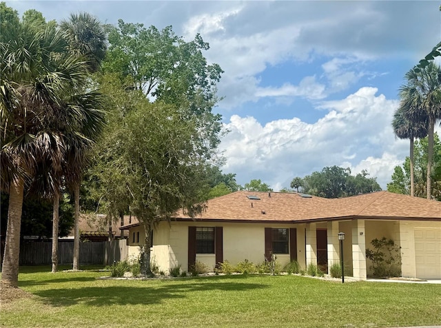 back of house with a garage, stucco siding, fence, and a lawn