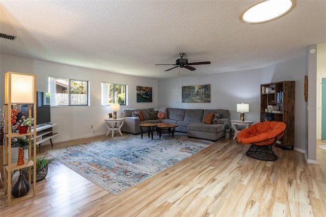 living area with ceiling fan, a textured ceiling, visible vents, wood finished floors, and baseboards