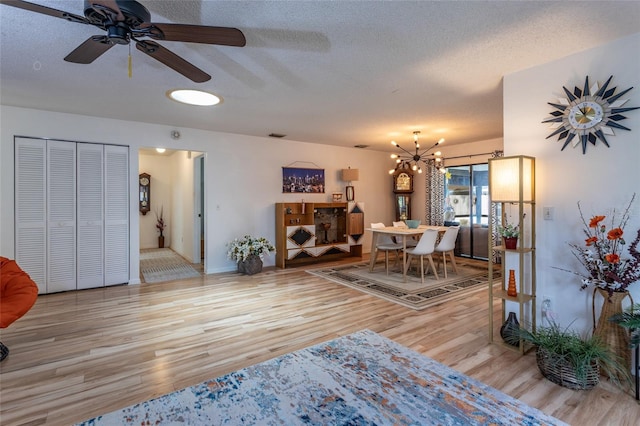 living room with light wood finished floors, visible vents, a textured ceiling, and ceiling fan with notable chandelier