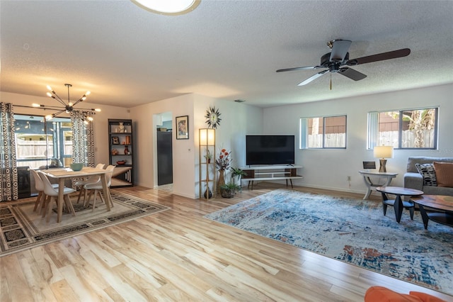living area with a textured ceiling, baseboards, ceiling fan with notable chandelier, and wood finished floors