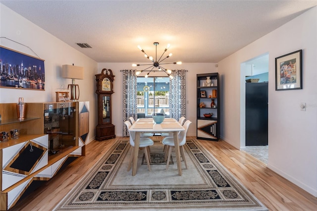 dining area with baseboards, light wood-type flooring, a chandelier, a textured ceiling, and visible vents