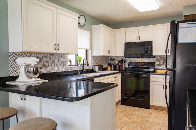 kitchen featuring a sink, dark countertops, a peninsula, black appliances, and white cabinetry