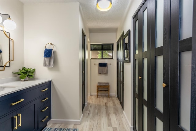 hall with baseboards, light wood finished floors, and a textured ceiling