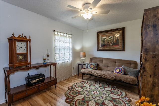 living area with ceiling fan, light wood-style floors, and a textured ceiling