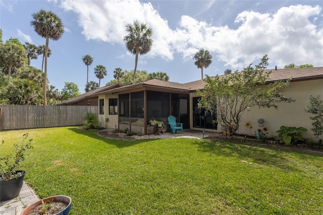 rear view of property with fence private yard, stucco siding, a sunroom, and a lawn