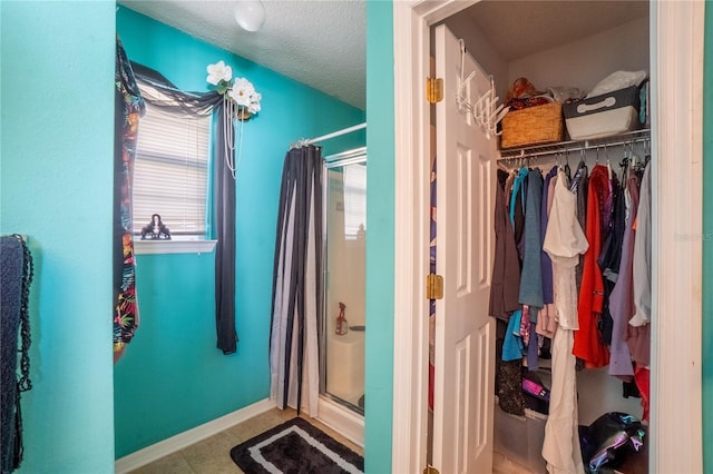 bathroom featuring a textured ceiling, a spacious closet, a stall shower, baseboards, and tile patterned floors