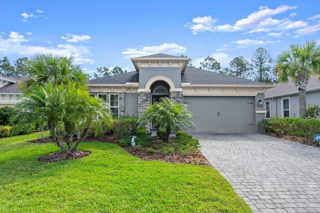 view of front of house with stucco siding, decorative driveway, a front yard, stone siding, and an attached garage
