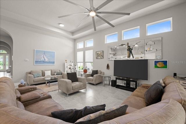 living room featuring ceiling fan, arched walkways, and a towering ceiling