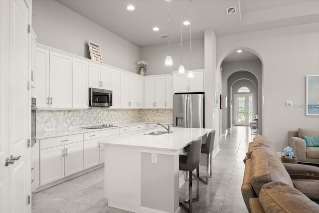 kitchen with tasteful backsplash, open floor plan, appliances with stainless steel finishes, arched walkways, and a sink