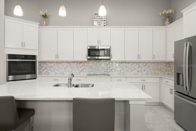 kitchen featuring white cabinets, a sink, stainless steel appliances, decorative backsplash, and a breakfast bar area