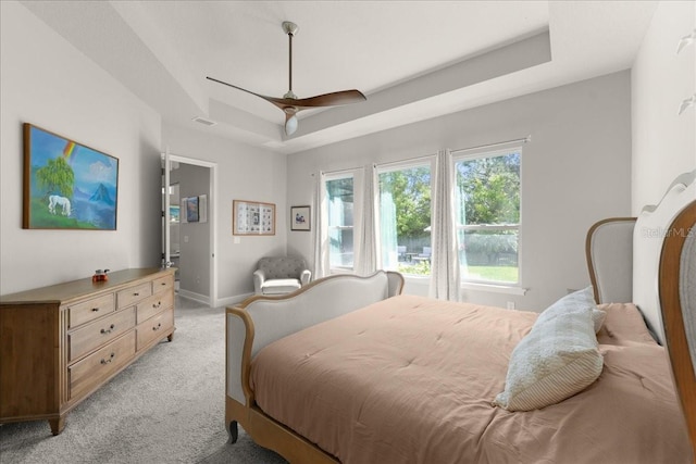 bedroom featuring visible vents, baseboards, a ceiling fan, a tray ceiling, and light carpet