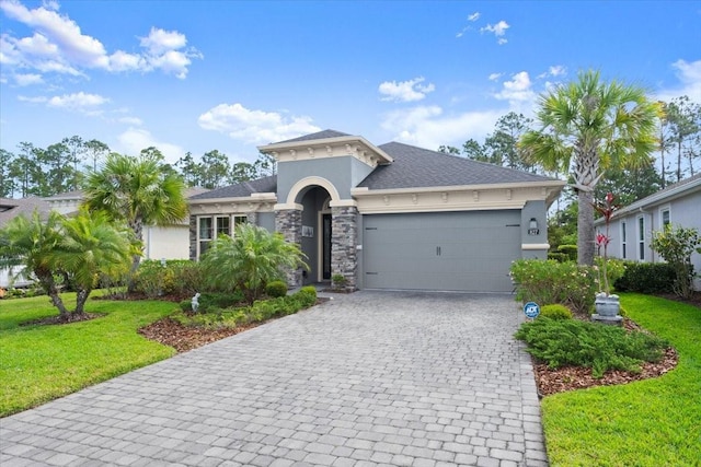 view of front of property featuring decorative driveway, roof with shingles, stone siding, a front lawn, and a garage