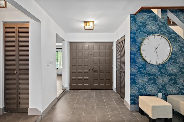 entrance foyer with baseboards, an accent wall, and wallpapered walls