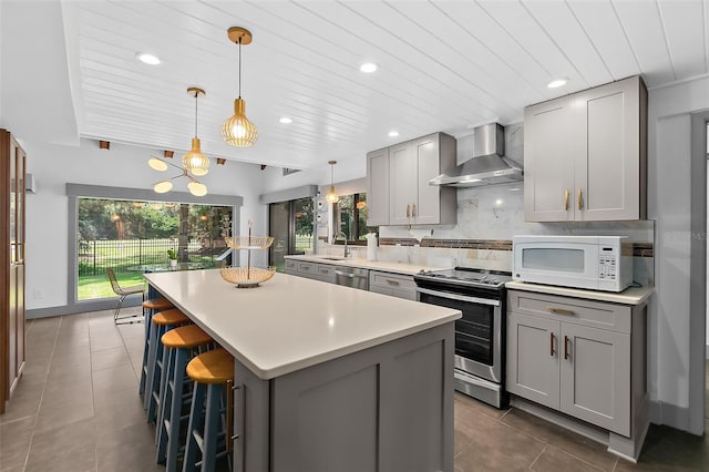 kitchen featuring tasteful backsplash, gray cabinets, a kitchen island, wall chimney exhaust hood, and stainless steel appliances