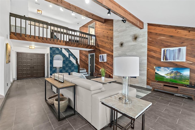 living room featuring track lighting, wooden walls, beamed ceiling, stairs, and high vaulted ceiling