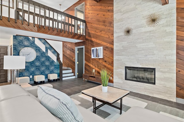 living area with wood walls, a stone fireplace, a high ceiling, and stairs