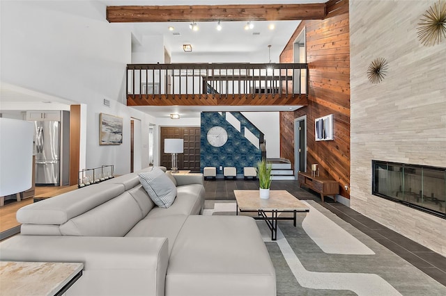 living area featuring a high ceiling, wooden walls, beamed ceiling, stairway, and a tile fireplace