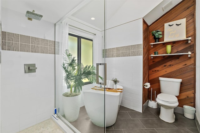 full bath featuring a freestanding bath, a tile shower, tile walls, toilet, and tile patterned floors