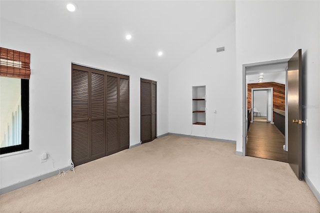 unfurnished bedroom with visible vents, two closets, recessed lighting, high vaulted ceiling, and carpet flooring