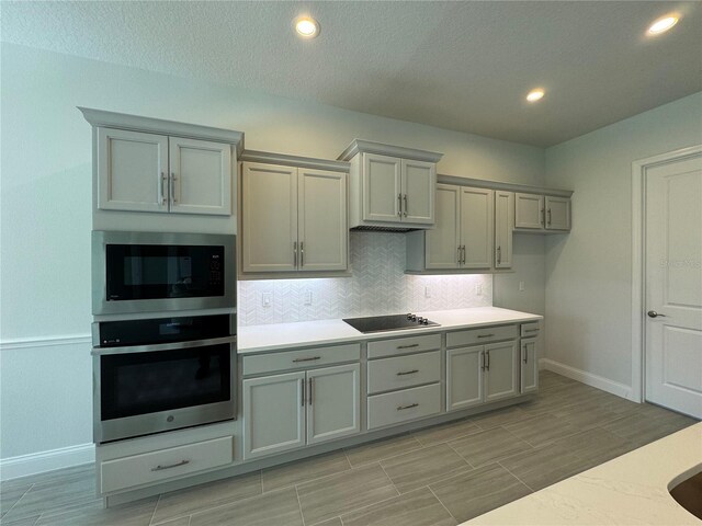1665 Lake Reserve Dr, Deland, FL 32724 - kitchen featuring oven, built in microwave, gray cabinetry, black electric stovetop, and baseboards