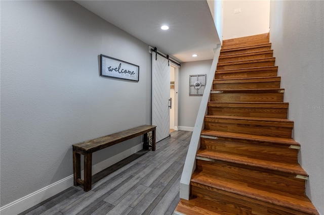 staircase with wood finished floors, recessed lighting, baseboards, and a barn door