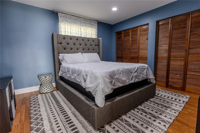 bedroom featuring recessed lighting, baseboards, multiple closets, and wood finished floors
