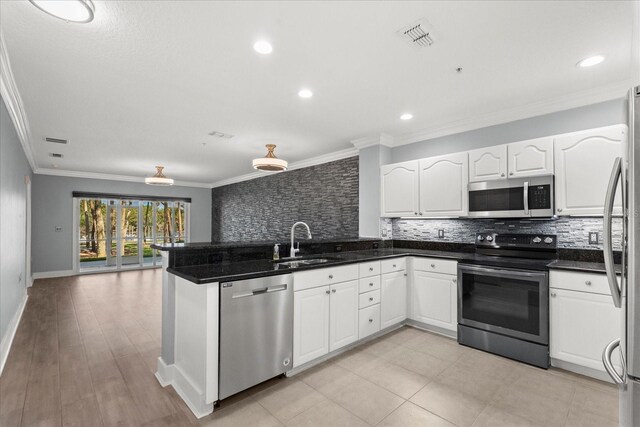 kitchen with appliances with stainless steel finishes, a sink, backsplash, a peninsula, and crown molding