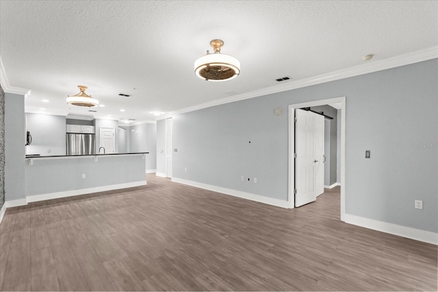 unfurnished living room with ornamental molding, wood finished floors, baseboards, a barn door, and recessed lighting