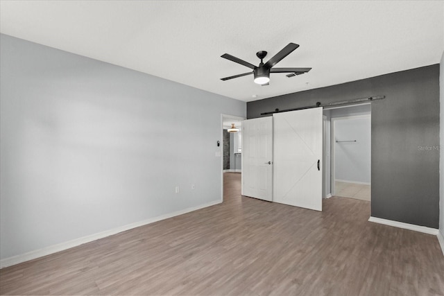 unfurnished bedroom with wood finished floors, a barn door, baseboards, and a ceiling fan