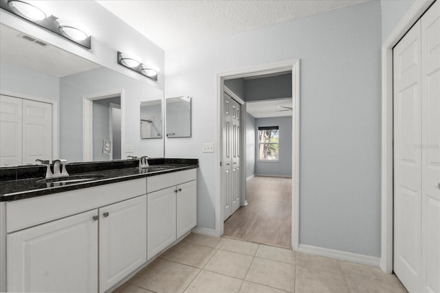 full bath featuring a closet, baseboards, double vanity, tile patterned flooring, and a textured ceiling