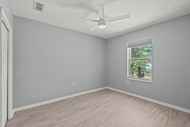 spare room featuring light wood-type flooring, a ceiling fan, baseboards, and a textured ceiling