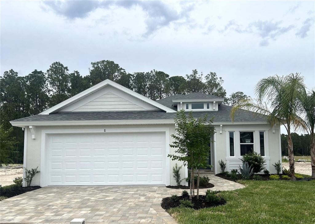 8 Juniper Ln, Palm Coast, FL 32164 - view of front of house featuring decorative driveway, a shingled roof, an attached garage, a front lawn, and stucco siding
