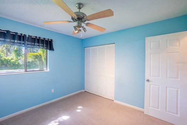 unfurnished bedroom featuring a closet, light carpet, baseboards, a textured ceiling, and a ceiling fan