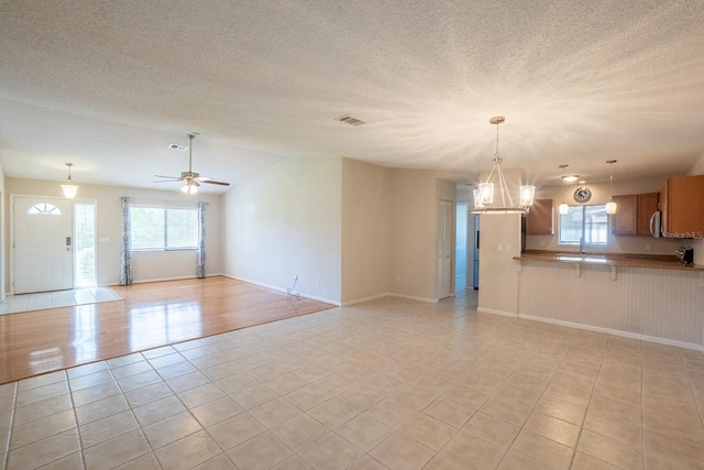 unfurnished living room with visible vents, a textured ceiling, ceiling fan with notable chandelier, and light tile patterned floors