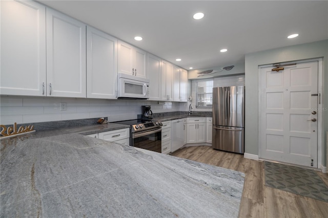 1155 Ocean Shore Blvd Unit 702, Ormond Beach, FL 32176 - kitchen featuring backsplash, light wood-type flooring, dark stone counters, appliances with stainless steel finishes, and white cabinetry