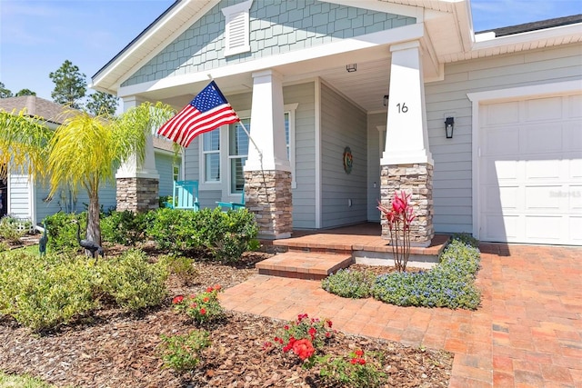 doorway to property featuring an attached garage, a porch, and stone siding