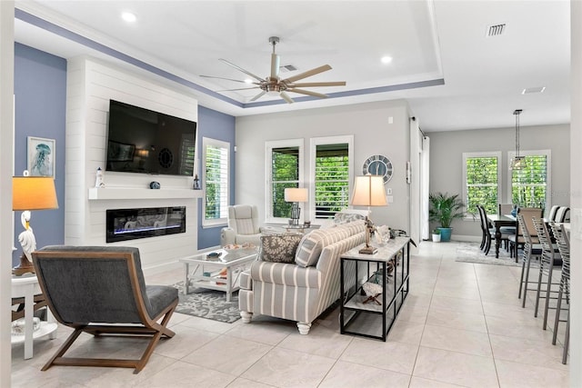 living area featuring a fireplace, a raised ceiling, ceiling fan, and light tile patterned floors