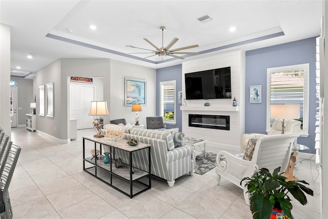 living room with a raised ceiling, visible vents, a ceiling fan, light tile patterned floors, and a large fireplace