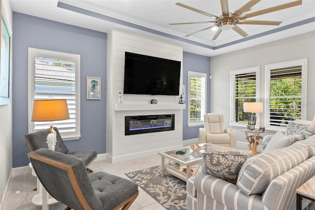 living area featuring baseboards, a ceiling fan, a tray ceiling, and a fireplace
