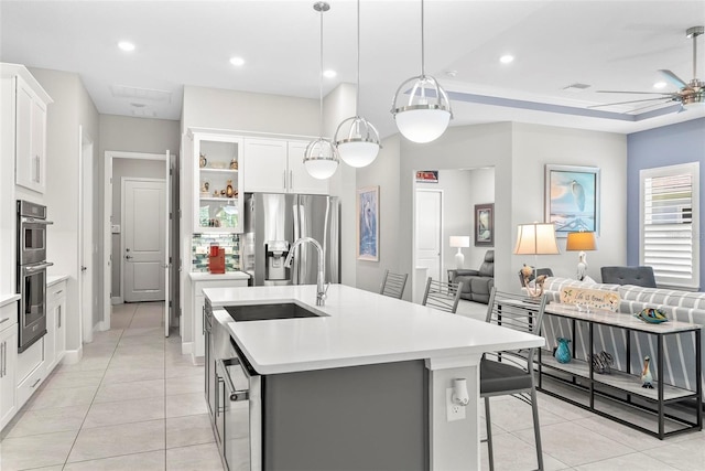 kitchen with stainless steel appliances, light tile patterned flooring, open floor plan, light countertops, and an island with sink