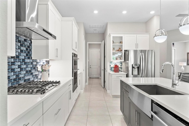 kitchen with wall chimney range hood, appliances with stainless steel finishes, a sink, and light countertops