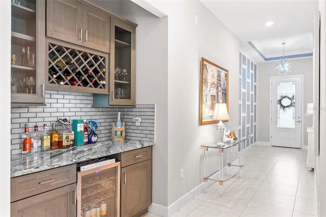 bar featuring beverage cooler, backsplash, a bar, light tile patterned floors, and baseboards