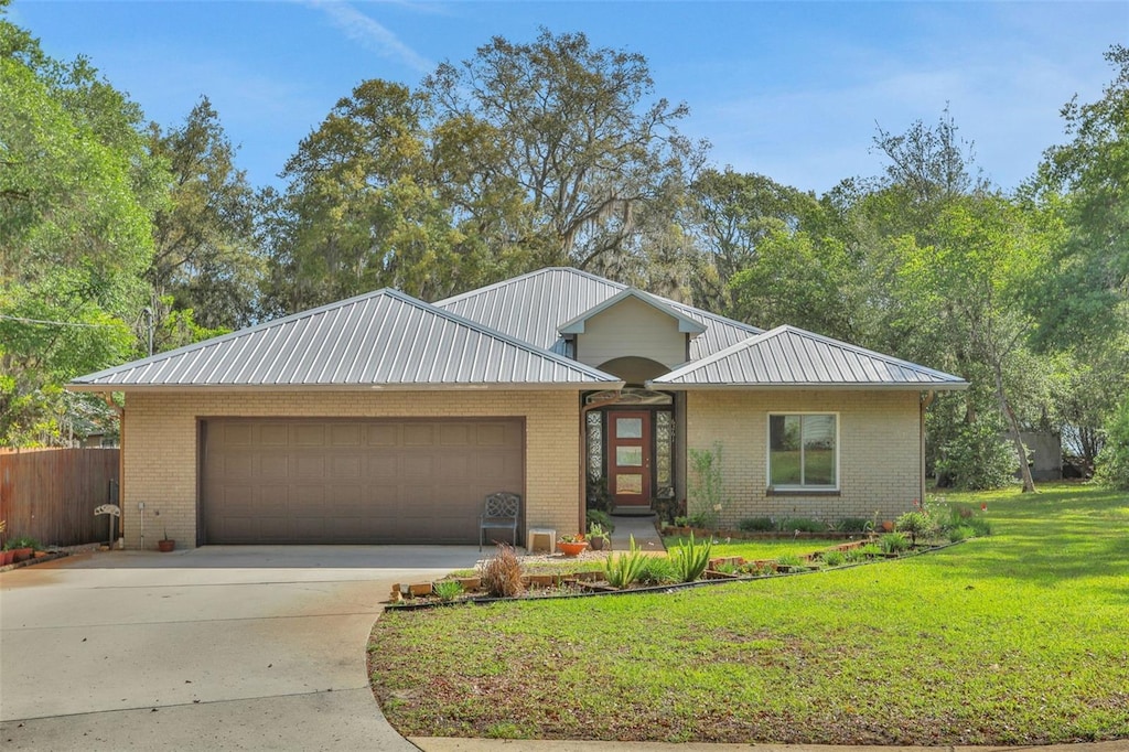 view of front facade with concrete driveway, a front lawn, an attached garage, metal roof, and brick siding
