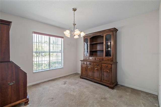 unfurnished dining area with light colored carpet, an inviting chandelier, and baseboards