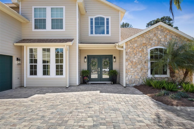 28 Cinnamon Grove Ln, Palm Coast, FL 32137 - doorway to property featuring french doors, a shingled roof, a garage, and stone siding