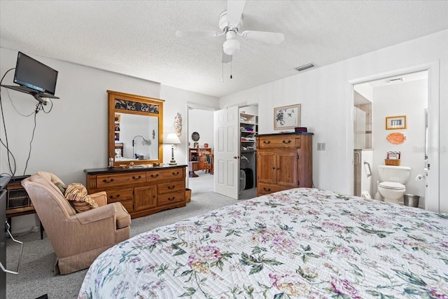 bedroom with a textured ceiling, connected bathroom, light colored carpet, visible vents, and a walk in closet